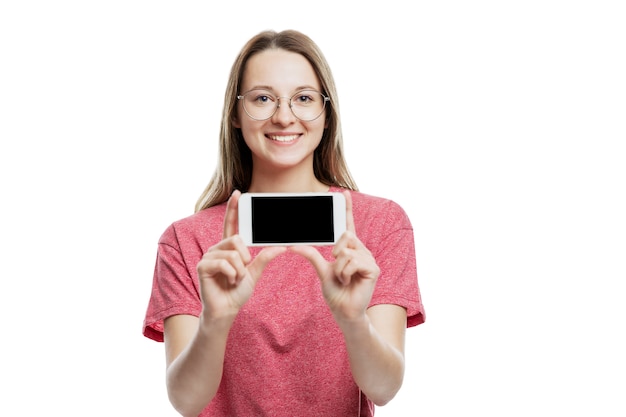 Smiling young girl shows smartphone isolated on black screen. Advertising and marketing. Space for text. White wall.