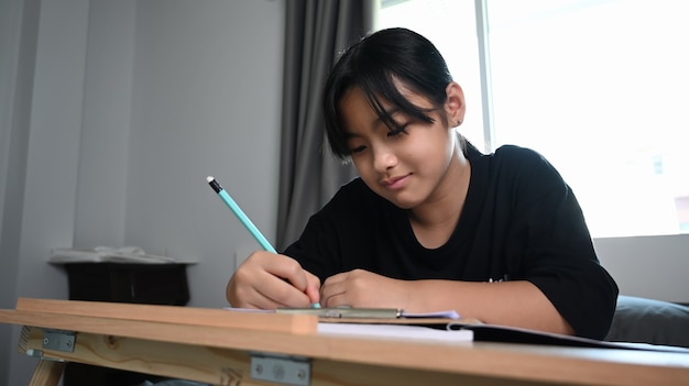 Smiling young girl in sitting on her bed and doing homework.