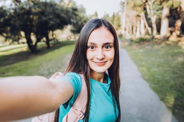 Smiling young girl wearing a turquoise t shirt  taking a POV selfie with her mobile in the park