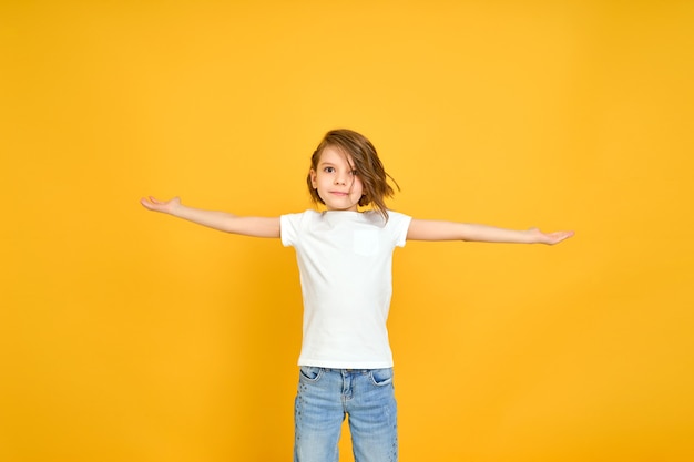 Smiling young girl in white t shirt with her arms opened isolated on yellow background