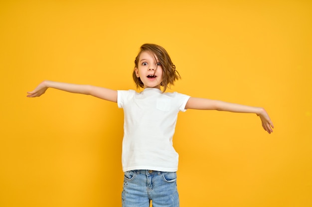 Smiling young girl in white t shirt with her arms opened isolated on yellow background