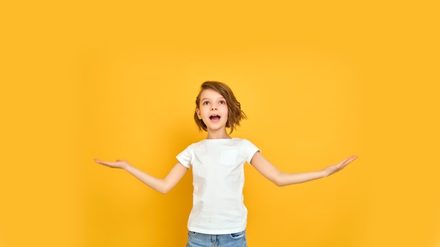 彼女の腕と黄色の背景で隔離の白いTシャツの笑顔の若い女の子