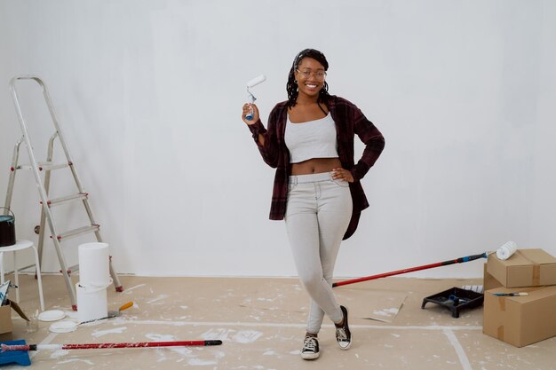 A smiling young girl with glasses and a paint roller in hand\
spends time in a renovated apartment