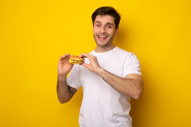 Smiling young guy holding burger at studio