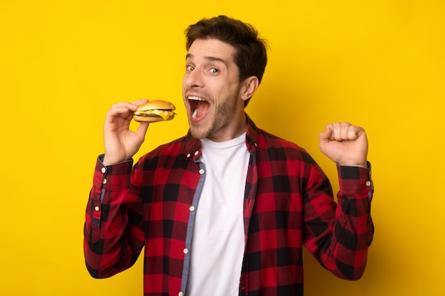 Smiling young guy holding burger at studio