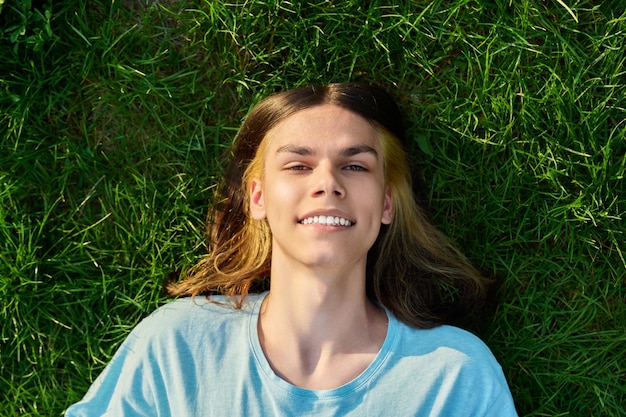 Smiling young guy looking at the camera lying on the grass