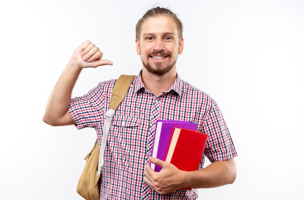 Smiling young guy student wearing backpack holding books points at himself