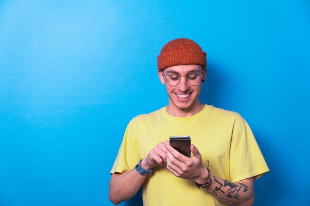 Photo smiling young guy with glasses using smartphone app in blue background