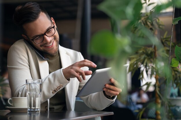 smiling young handsome business man sitting in cafe sharing business ideas with colleague over mobile phone while using fintech technology device
