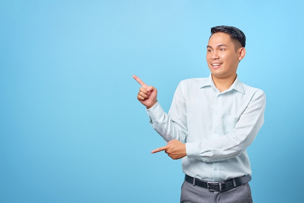 Smiling young handsome businessman pointing finger away at copy space on blue background