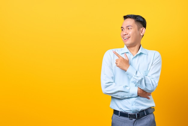 Smiling young handsome businessman pointing finger away at copy space on yellow background