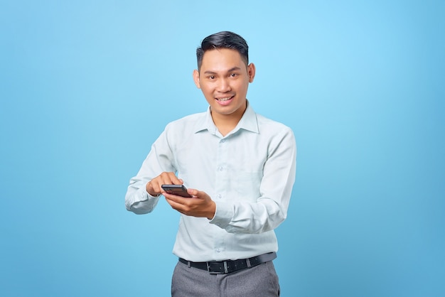 Smiling young handsome businessman using and texting smartphone on blue background