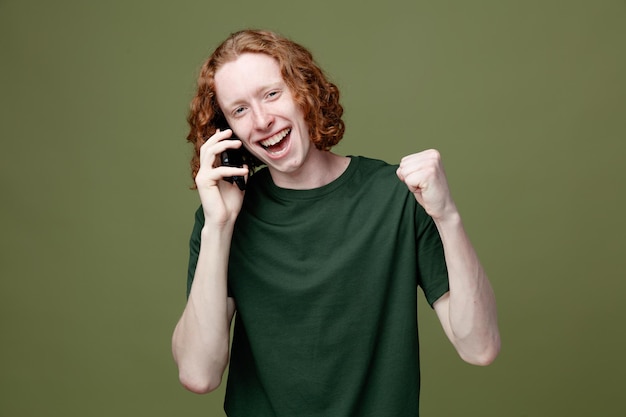 Smiling young handsome guy wearing green t shirt speaks on phone isolated on green background