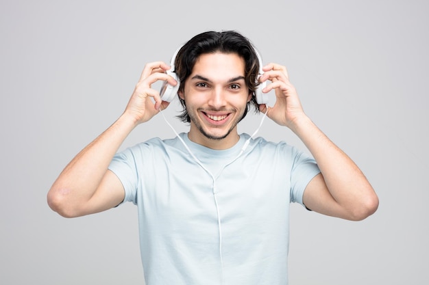 smiling young handsome man looking at camera taking headphones off isolated on white background