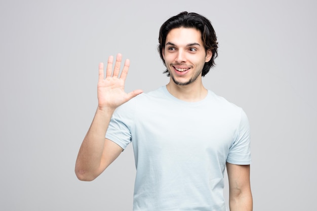 Smiling young handsome man looking at side showing hi gesture isolated on white background