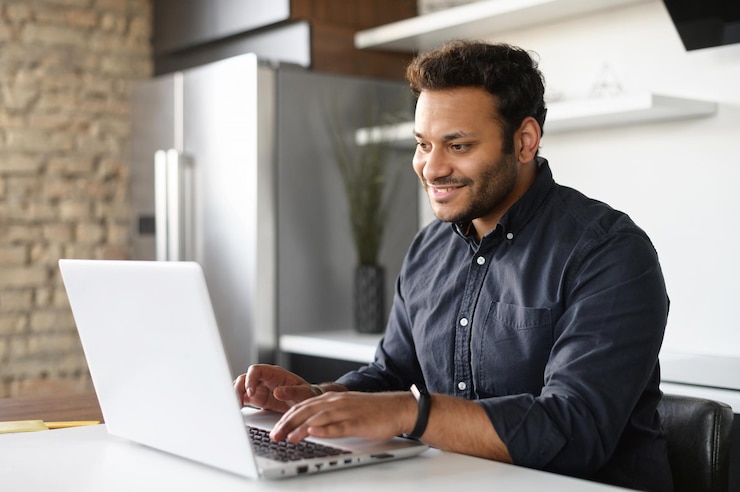 Photo smiling young indian guy using a laptop for remote work from home