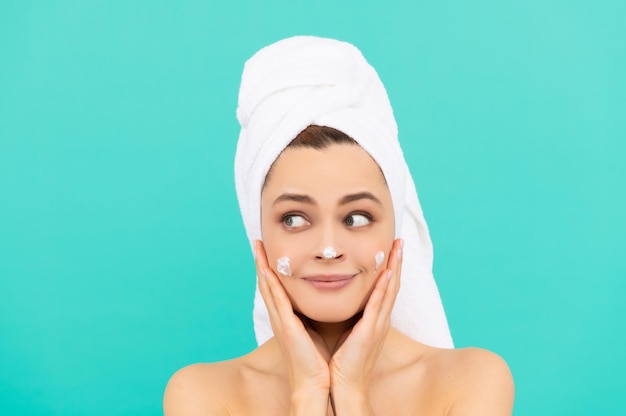 Photo smiling young lady applying face cream on blue background