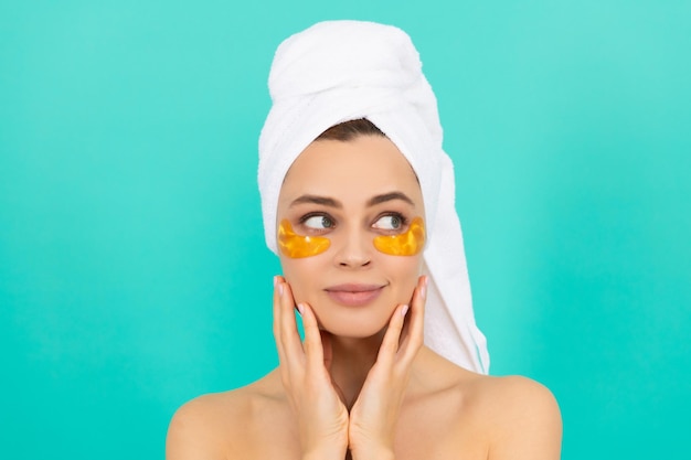 Smiling young lady has collagen golden eye patches on face with towel