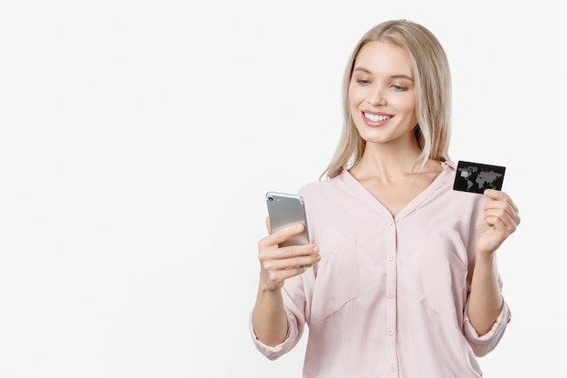 Smiling young lady isolated over white background using mobile phone holding credit card