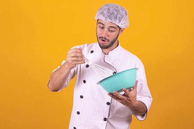 Smiling young male chef cook or baker man in white uniform\
shirt posing isolated on yellow background studio portrait cooking\
food concept mock up copy space whipping beating eggs in bowl