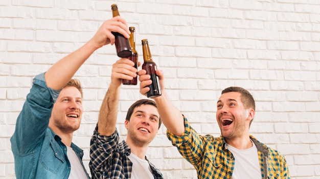 Smiling young male friends standing against white wall raising toast