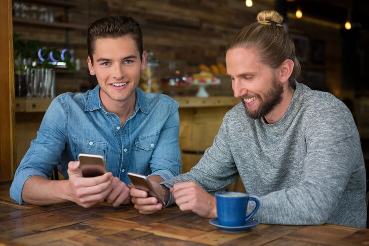 Smiling young male hipsters using smart phones at table in coffee shop