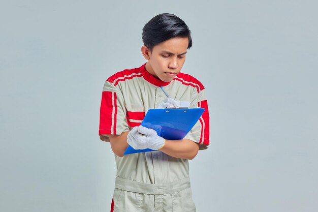 Smiling young male mechanic taking notes on clipboard on gray background