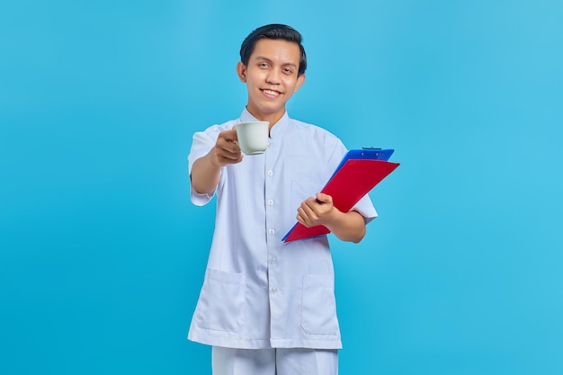 Smiling young male nurse holding folder and cup over blue background