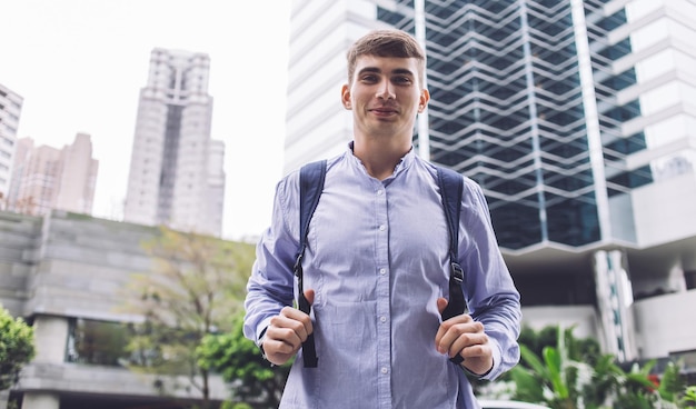 smiling young male traveler and papers looking at camera in downtown around modern buildings