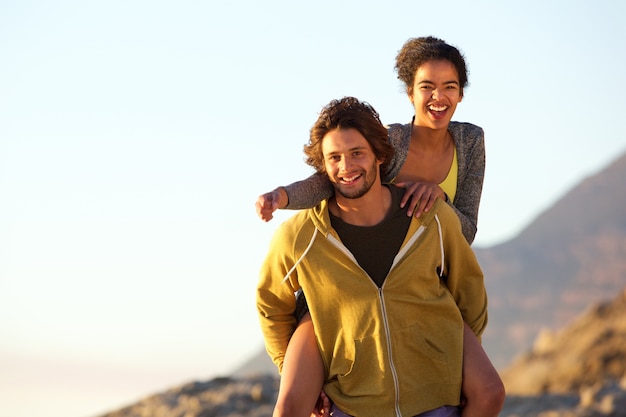 Smiling young man carrying carefree woman on back