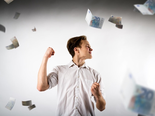 Photo smiling young man celebrating success while gesturing by paper currency against white background