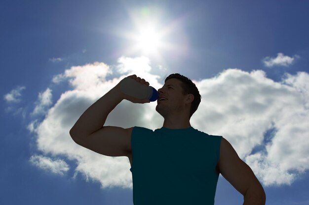 写真 雲と太陽と青い空を背景に笑顔の若い男が水を飲む