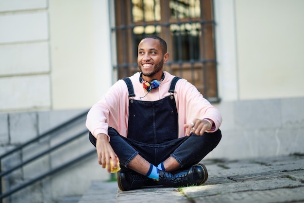 smiling young man eating apple while sitting on footpath