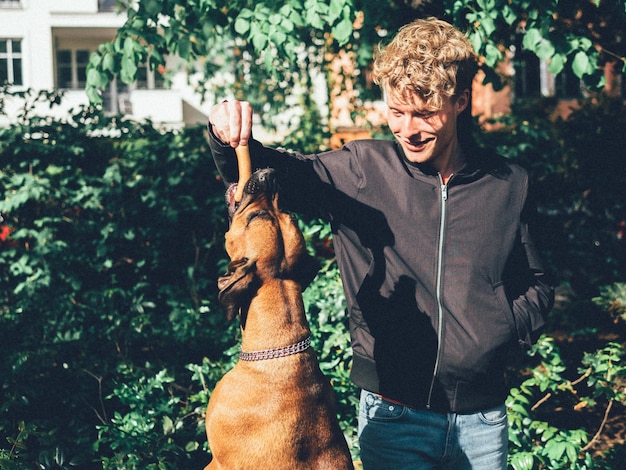 Photo smiling young man feeding sausage to dog in yard