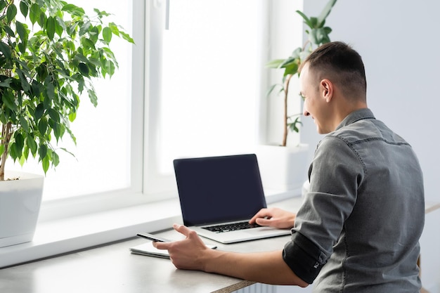 Photo smiling young man freelancer using laptop, studying online, working from home, happy casual guy typing on pc notebook surfing internet, enjoying distant job, sit at table.