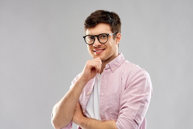 Улыбающийся молодой человек в очках на сером фоне