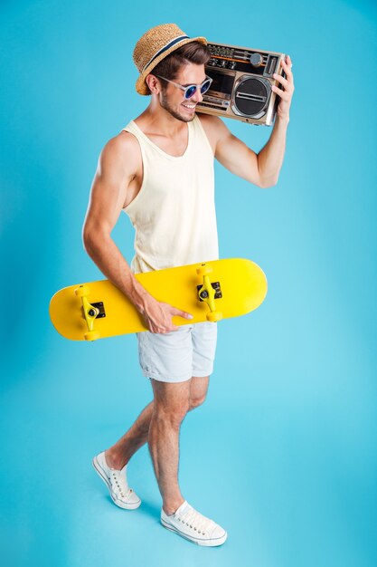 Smiling young man holding radio and yellow skateboard