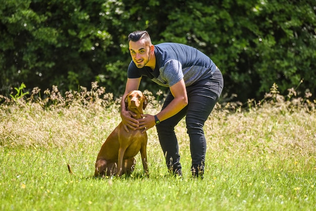 Photo smiling young man holding vizsla on grassy field