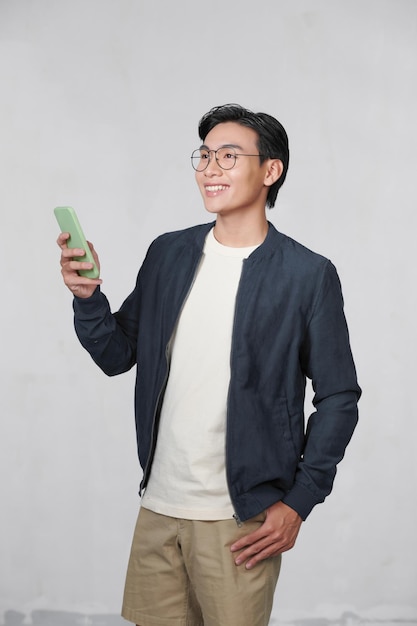 Smiling young man looking at his smart phone while text messaging isolated on white background