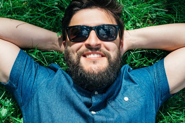 Smiling young man lying and relaxing on green grass