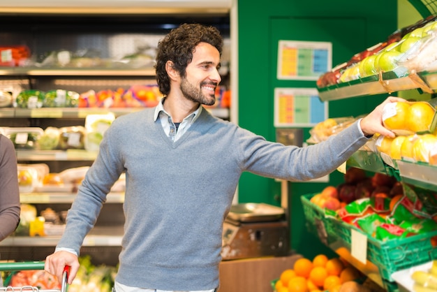 Smiling young man picking up vegetables in a grocery store