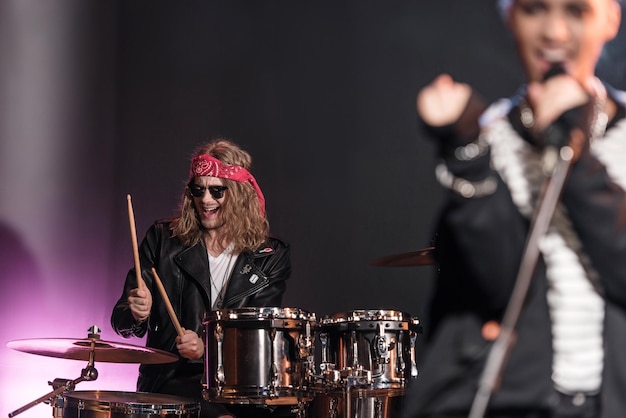 Smiling young man playing drums set with singer on stage