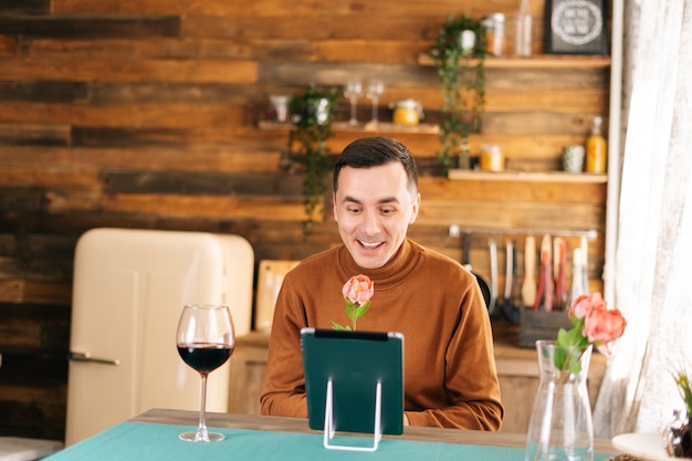 Smiling young man presents beautiful flower through tablet to his girlfriend during online communication. Male using tablet computer and having online video chat.