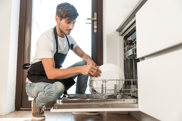 Smiling young man pulls out clean dishes from the dishwasher