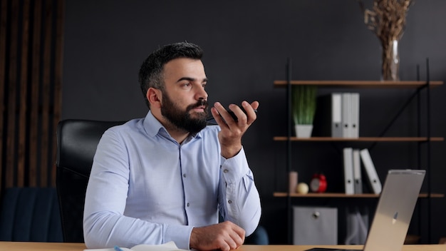 Smiling young man recording voice message on smartphone.Voice recognition, audio messages, using translator on mobile phone