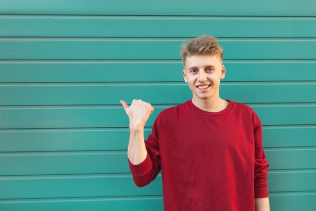 Photo smiling young man shows a hand on copyspace.