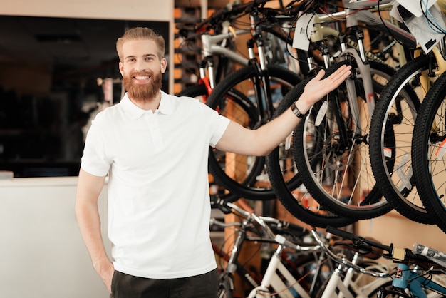 Il giovane sorridente mostra la fila delle biciclette moderne