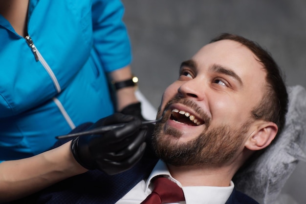 Улыбающийся молодой человек сидит в кресле стоматолога, пока врач осматривает его зубы