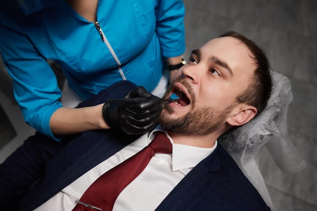 Smiling young man sitting in dentist chair while doctor examining his teeth