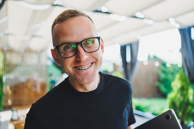 Photo a smiling young man stands on a summer terrace in a cafe with a laptop in his hands work online freelancer remote summer job online